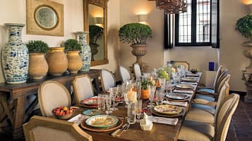 Uma sala de jantar com uma mesa de madeira comprida posta para uma refeição, rodeada de cadeiras.