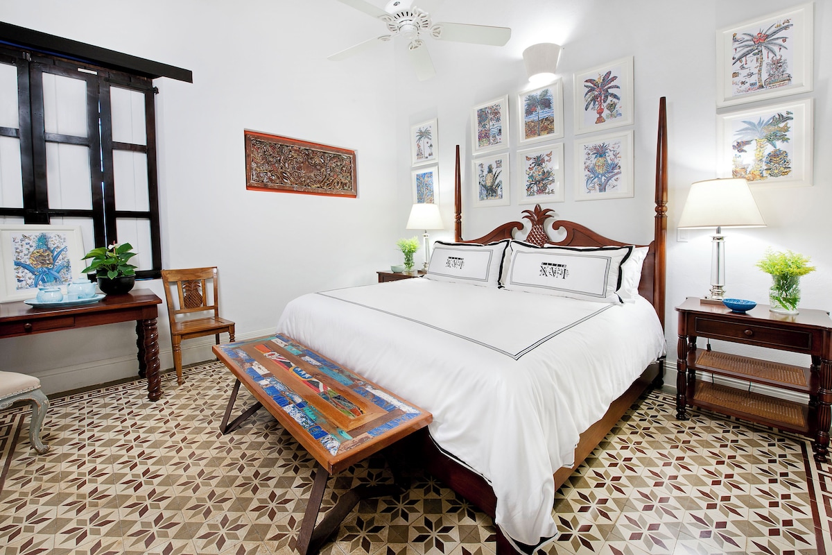 A bedroom with a large bed, a wooden chair, a small table, and a bench.