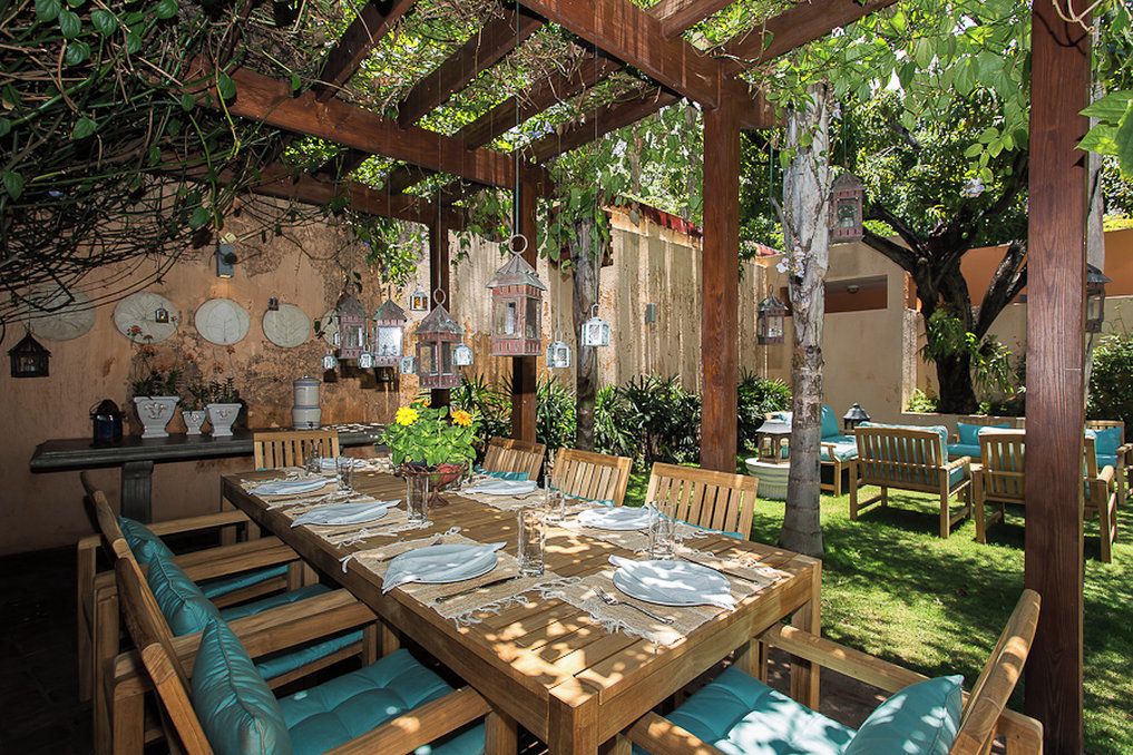 An outdoor dining area with a wooden table set for four, surrounded by wooden chairs with cushions.