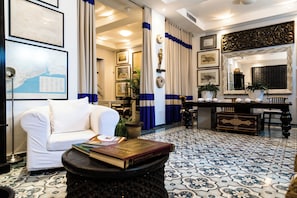A well-lit room with a white sofa, a coffee table with a book, a dining table with chairs, and a patterned floor.