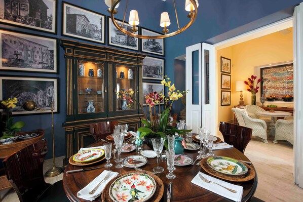 Un coin repas avec une table ronde dressée pour quatre personnes, entourée de photographies en noir et blanc encadrées, d’un meuble avec des portes en verre et d’un lustre.