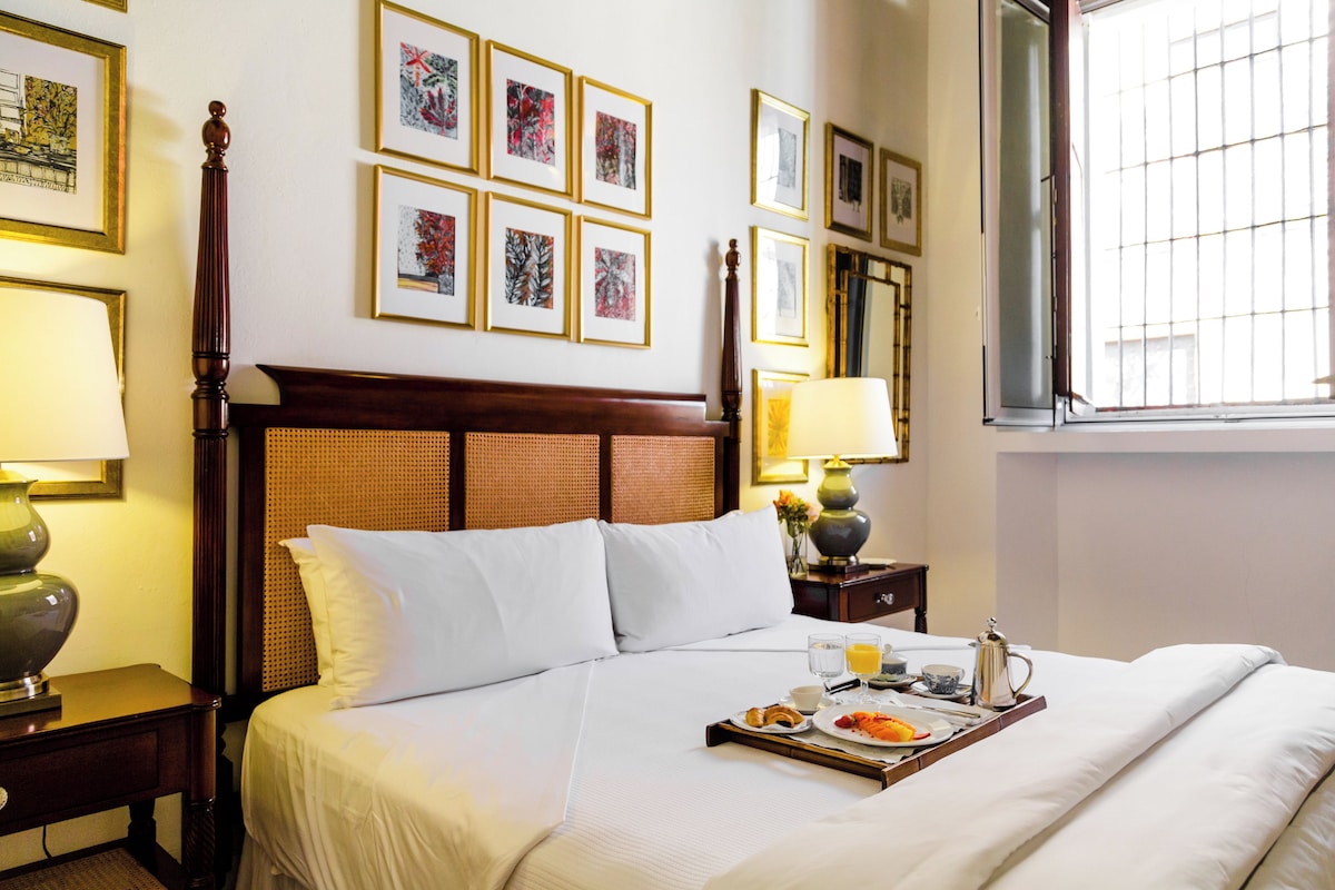 A hotel room with a bed, bedside lamps, a tray of breakfast, and framed artwork on the wall.