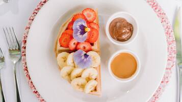 A plate with a slice of pizza topped with tomatoes, basil, and a flower, accompanied by a small bowl of sauce and a cup of tea.