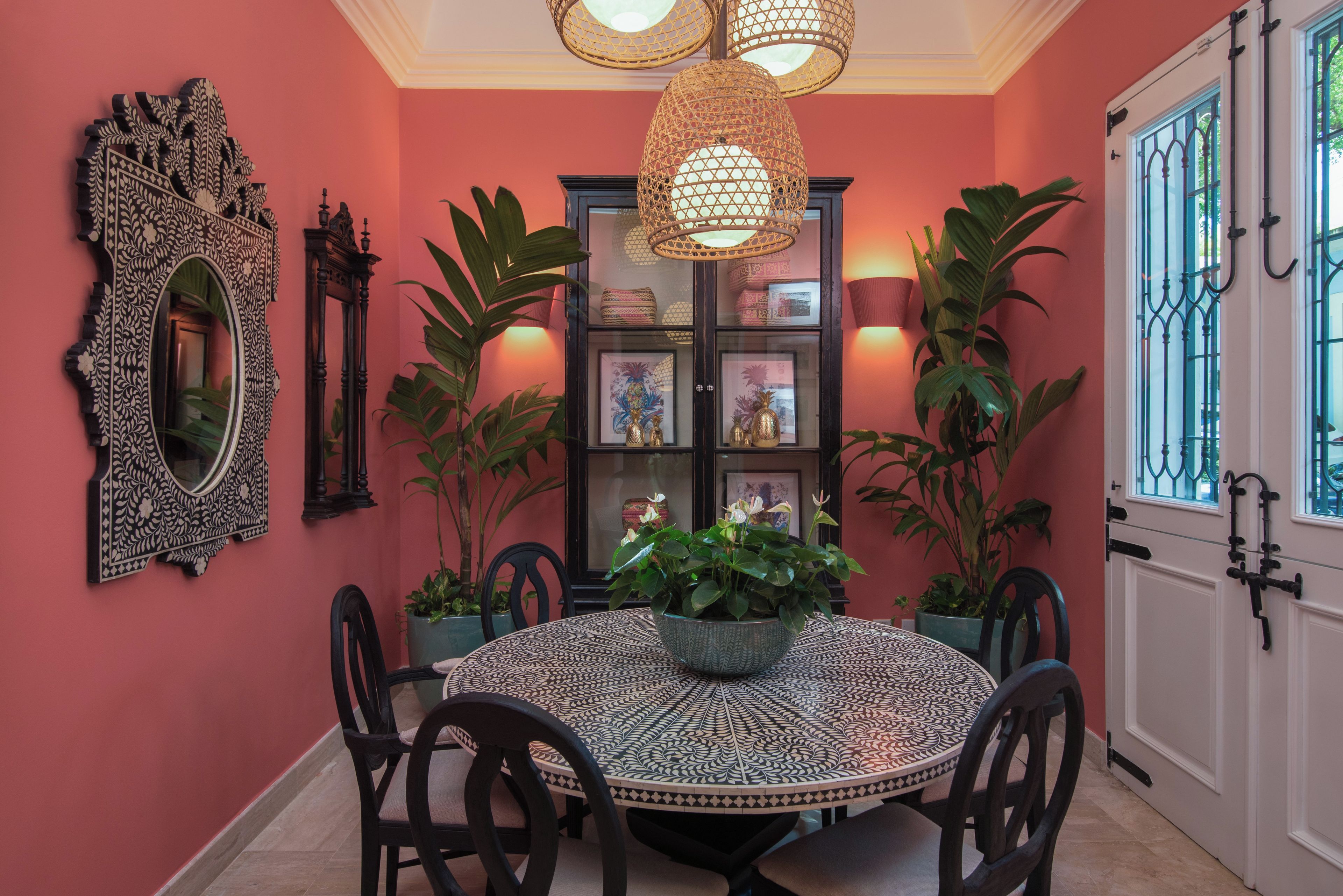 Uma sala de jantar com uma mesa redonda, cadeiras, um espelho decorativo e uma prateleira com molduras.