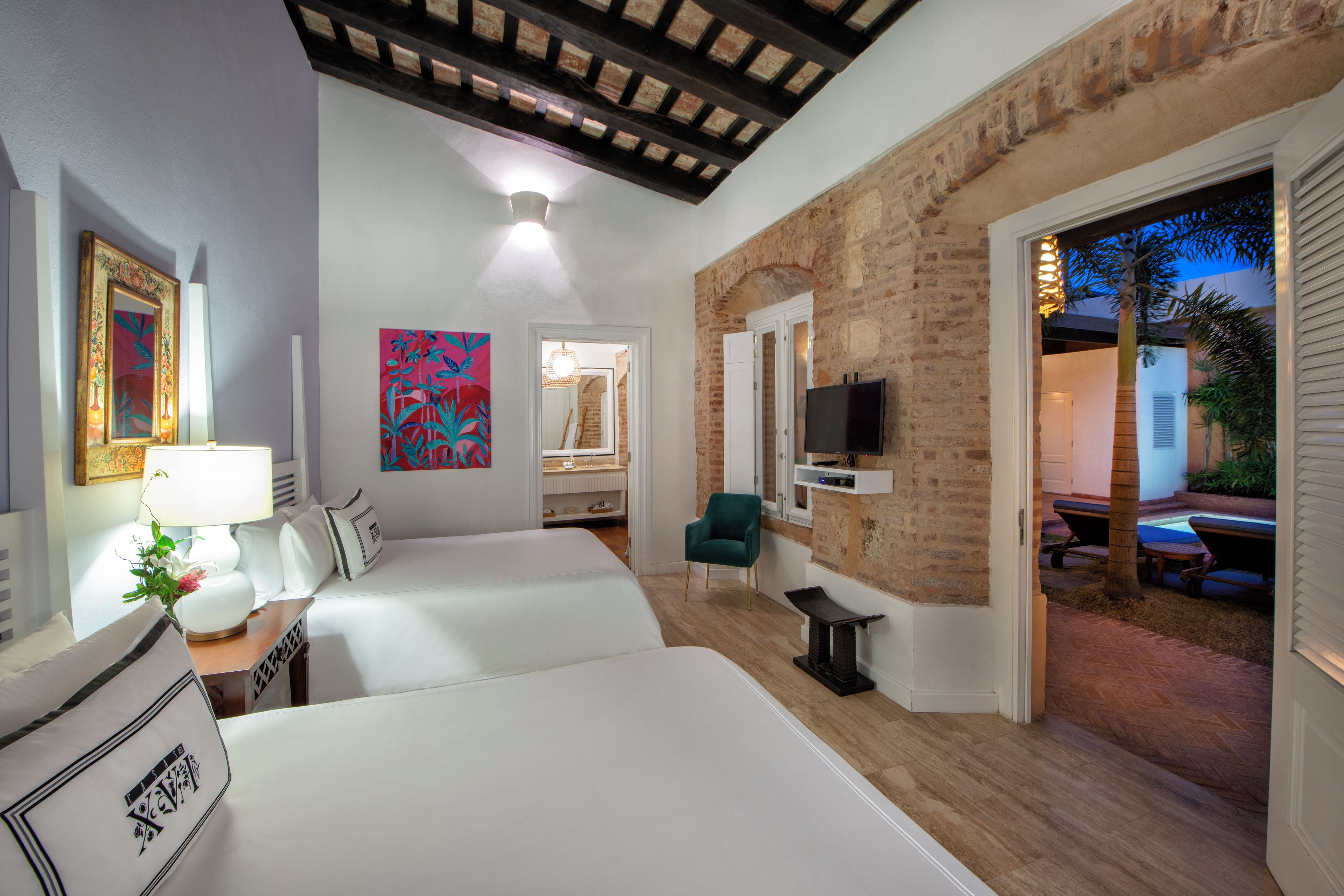 A hotel room with two beds, a TV, a desk with a lamp, and a painting.