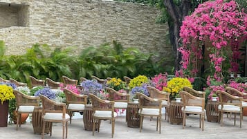 Mobiliario exterior con sillas y cojines de mimbre, rodeado de macetas con plantas y flores.