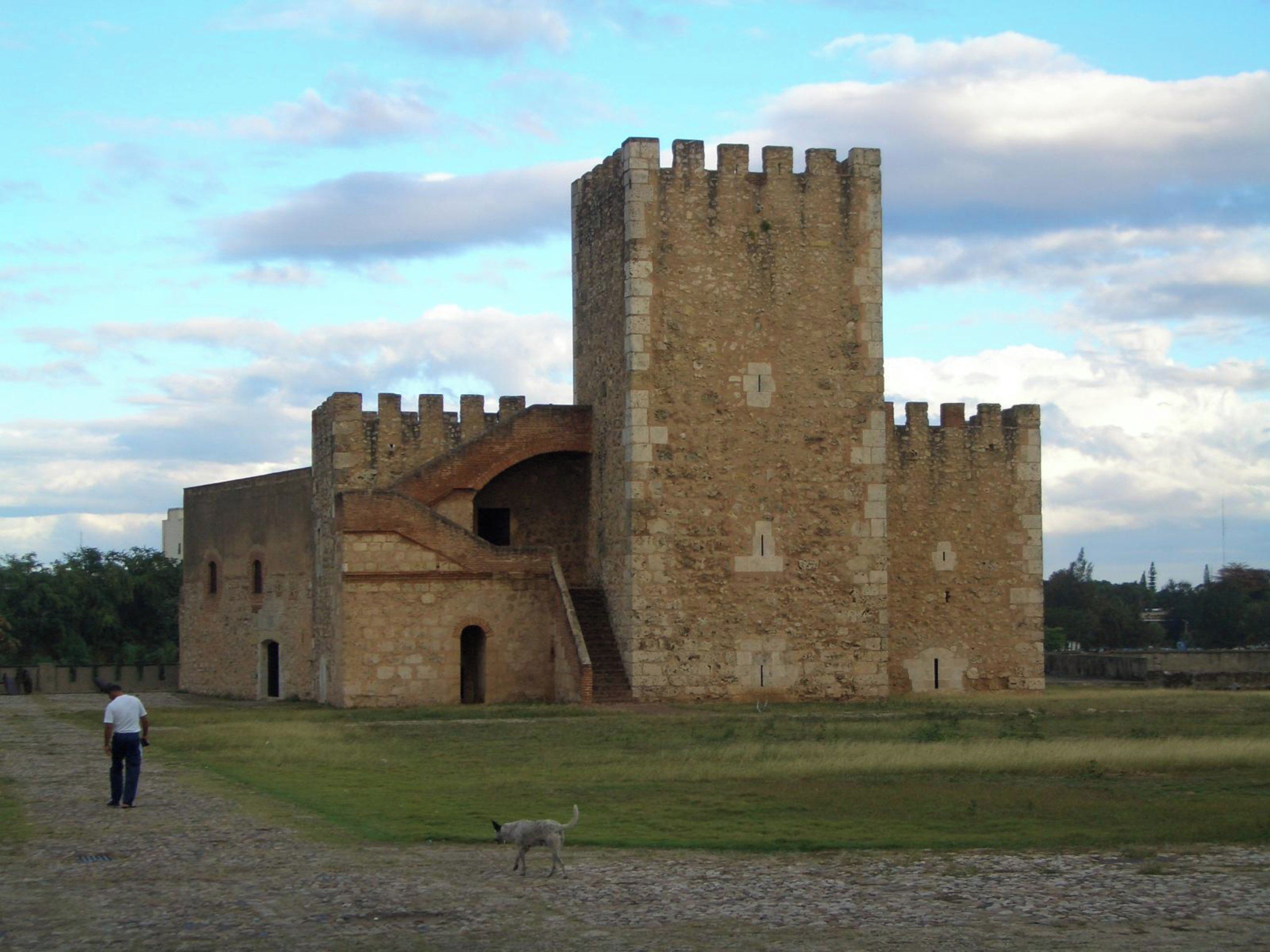 A historic stone castle with a prominent tower, a grassy courtyard, and a paved path.