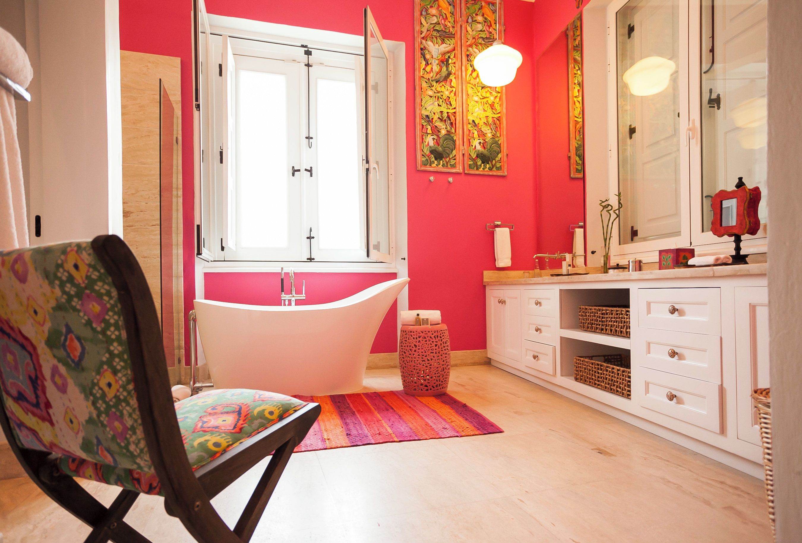 A bathroom with a freestanding bathtub, a white vanity with drawers, a mirror, and a colorful rug.