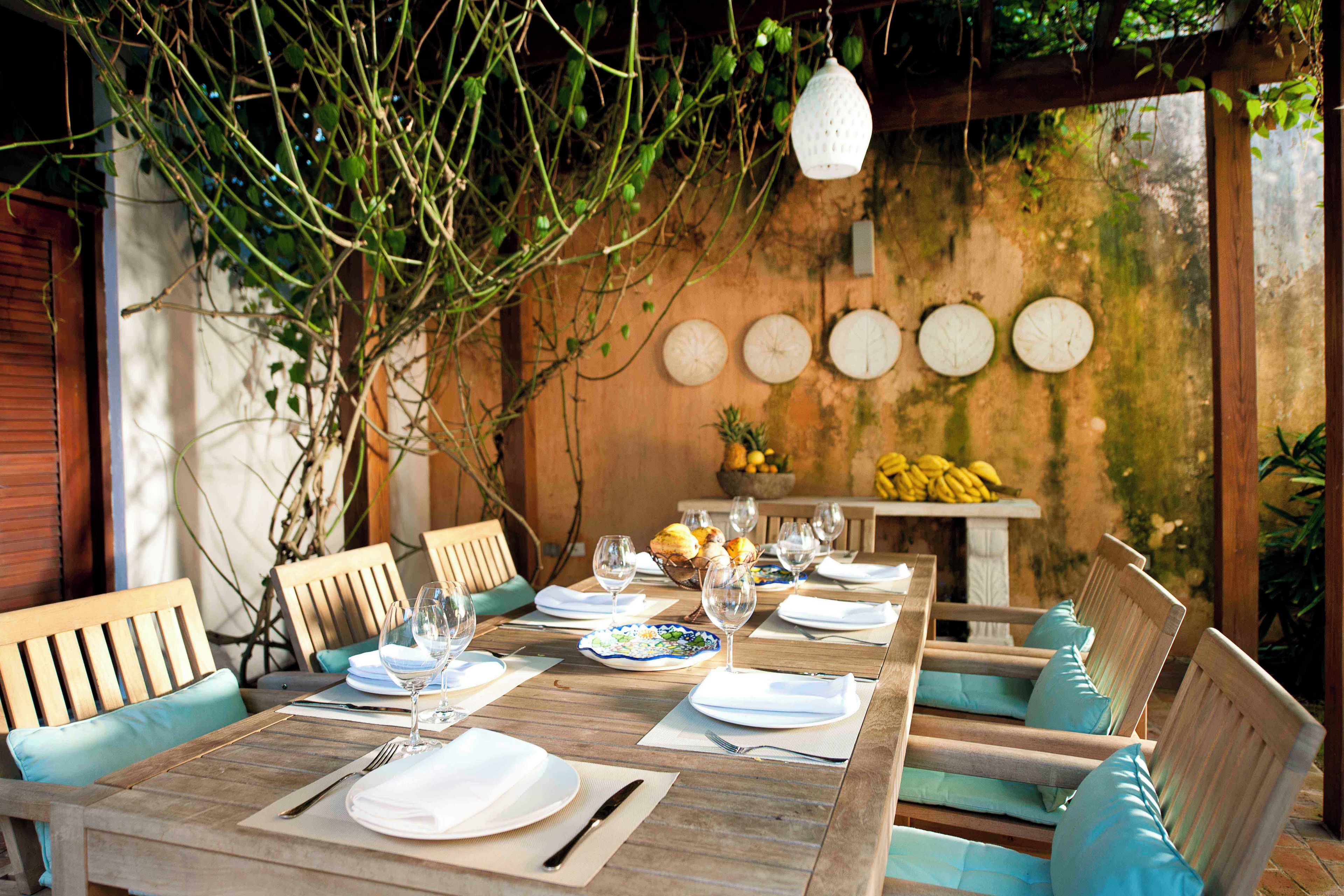 Un espace de restauration en plein air avec des tables et des chaises en bois, un luminaire suspendu et un mur orné de motifs circulaires.