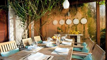 Un espace de restauration en plein air avec des tables et des chaises en bois, un luminaire suspendu et un mur orné de motifs circulaires.