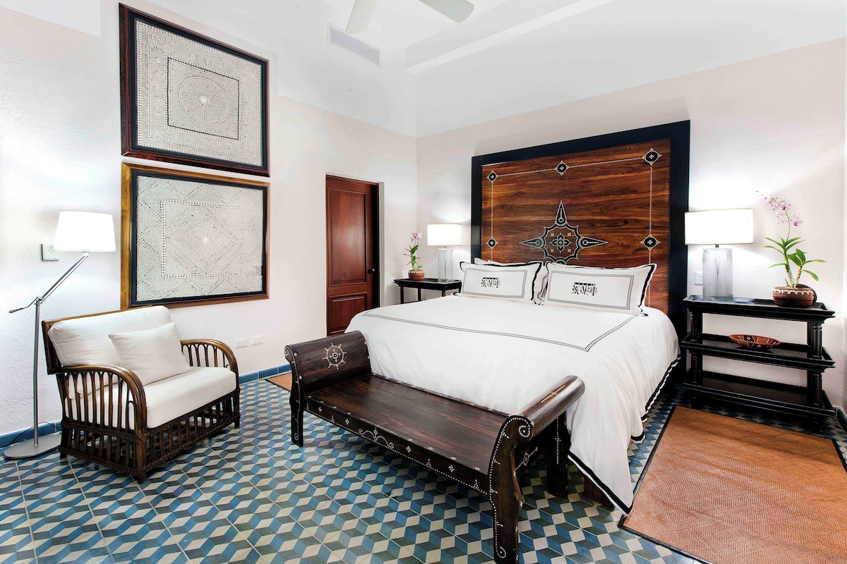 A hotel room with a large bed, a bench, a desk, and a chair.