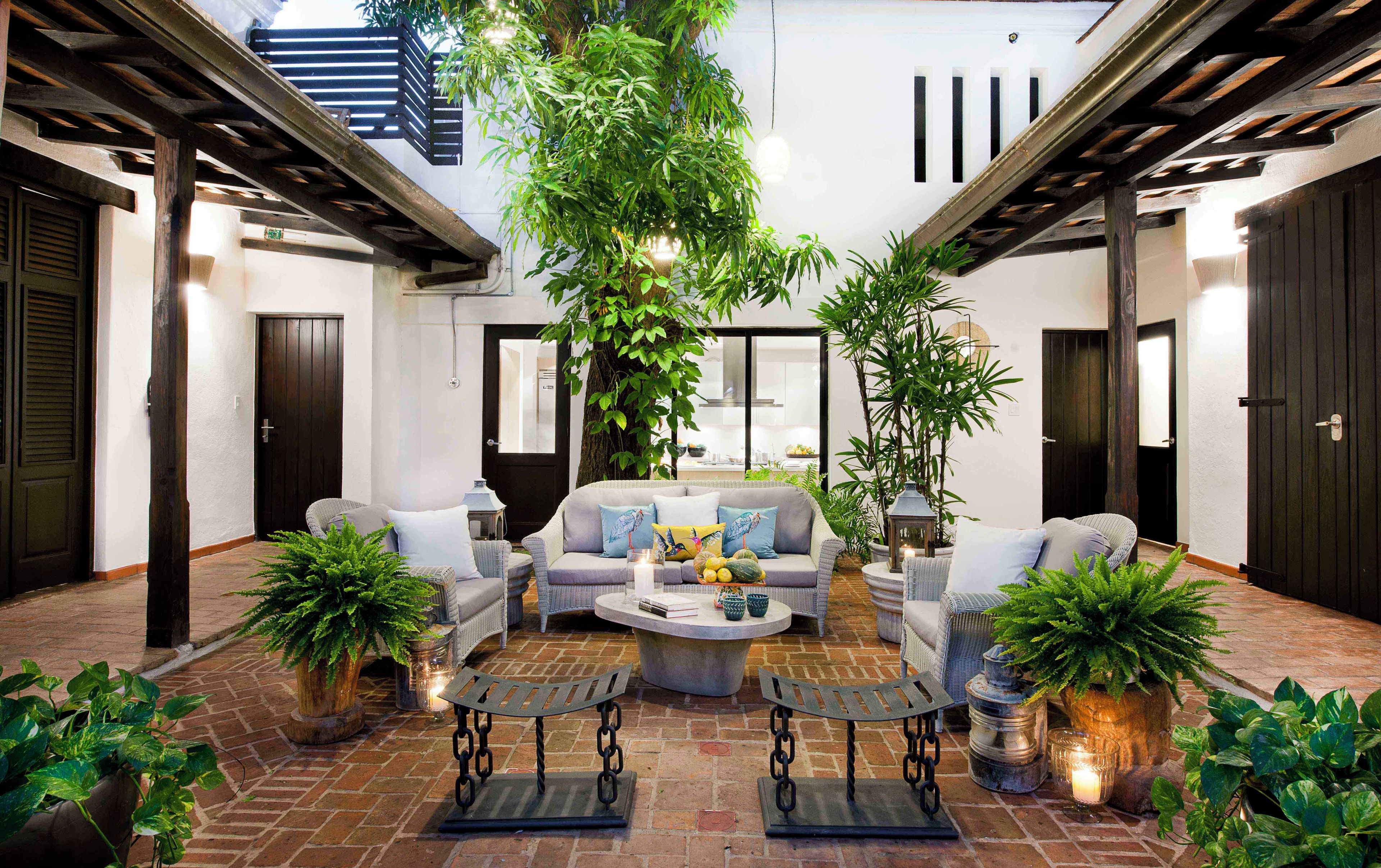 An outdoor seating area with a sofa, chairs, and a coffee table, surrounded by potted plants and a brick floor.
