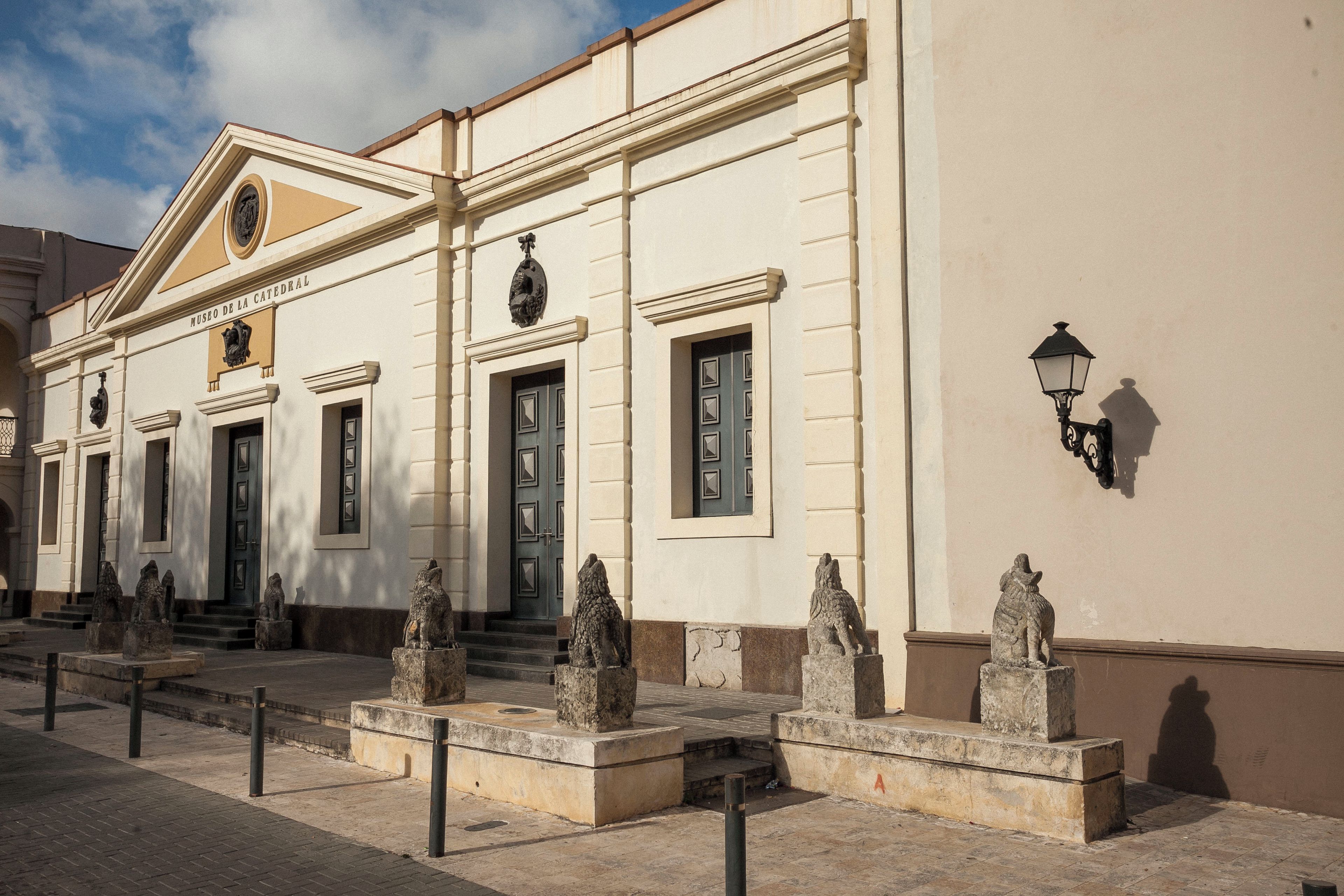 A building with a classical architectural style, featuring a central entrance with steps, flanked by statues and a street lamp.