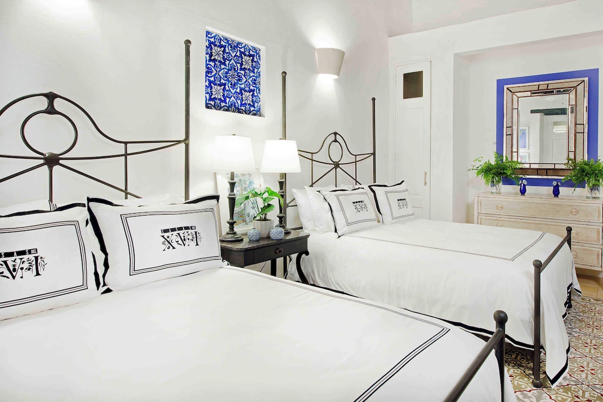 A hotel room with two beds, a nightstand with lamps, a dresser, and a mirror.