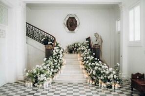 Un magnifique escalier, agrémenté de compositions florales blanches et de bougies, mène à un palier où se trouve une sculpture en buste.