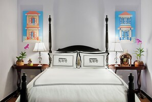 Een bed met een witte spreideken, twee zwarte nachtkastjes met lampen, een spiegel en een vaas met bloemen.