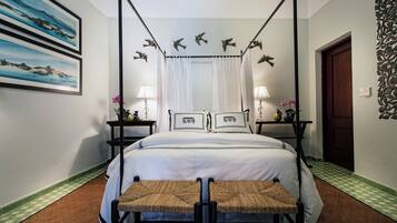 A four-poster bed with a canopy, two bedside tables with lamps, a bench, and artwork on the walls.