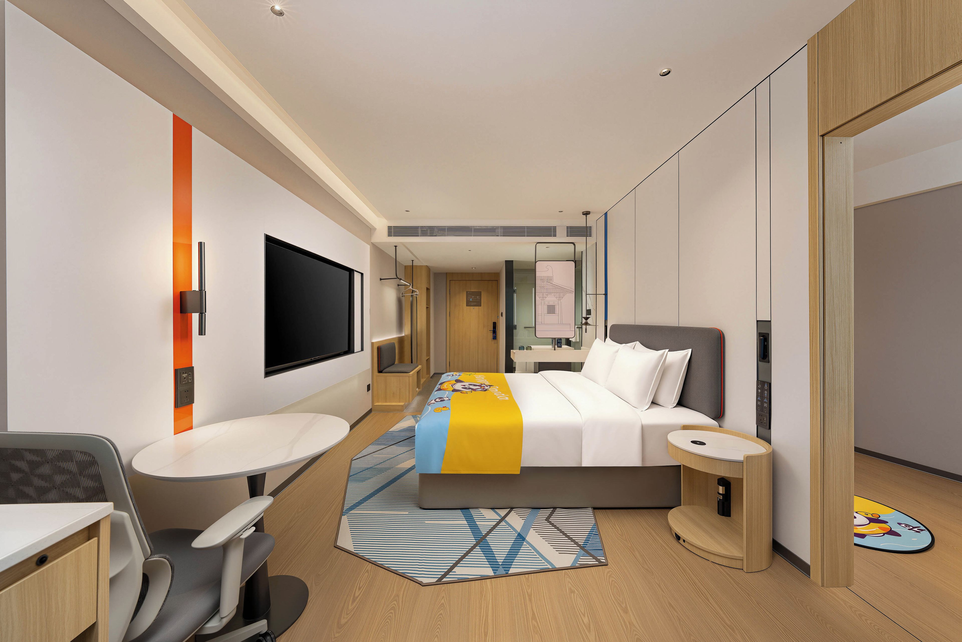 Ein modernes Hotelzimmer mit Bett, Nachttisch, Schreibtisch, Stuhl und einem Flachbildfernseher.
