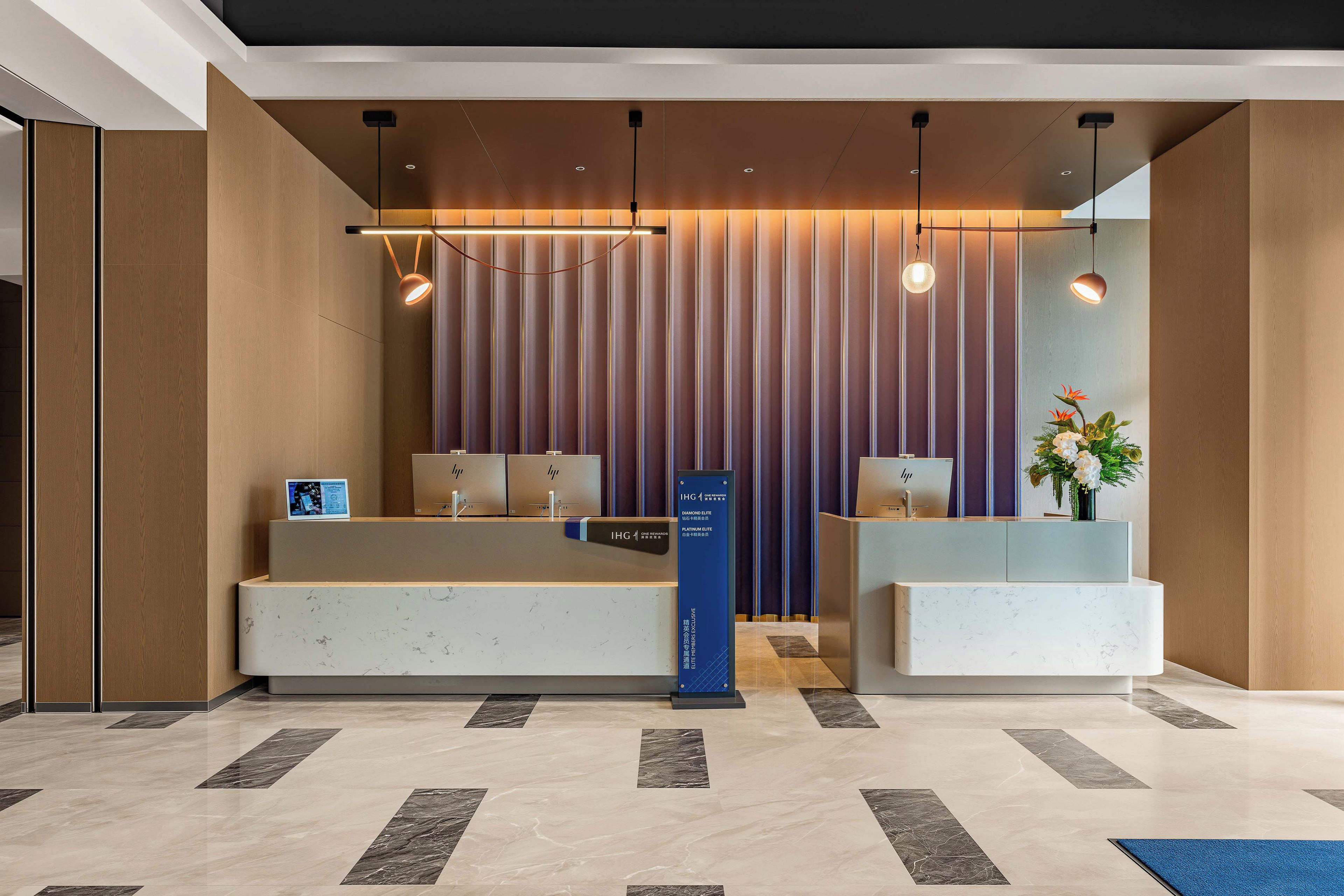 Ein Hotel-Rezeptionsbereich mit modernem Design, der einen Empfangstresen, eine digitale Infotafel und eine Rezeption beinhaltet.