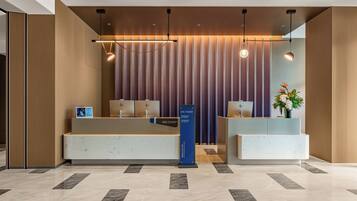 Ein Hotel-Rezeptionsbereich mit modernem Design, der einen Empfangstresen, eine digitale Infotafel und eine Rezeption beinhaltet.