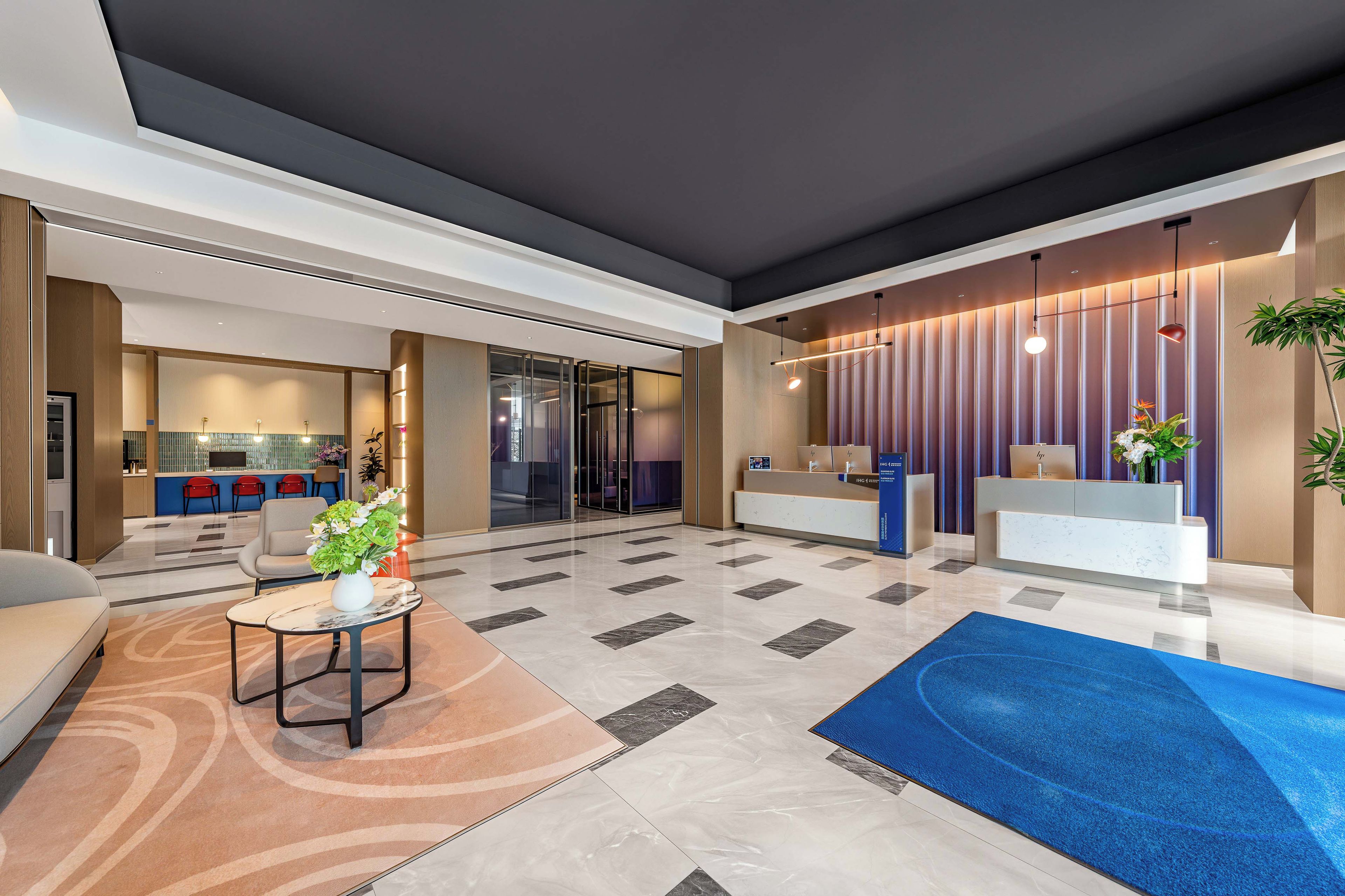 Un moderno vestíbulo de hotel con mostrador de recepción, zona de estar y alfombra azul.