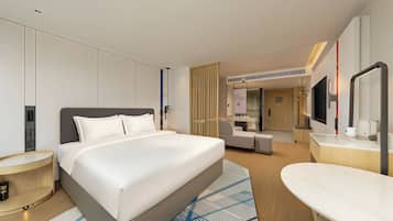 Una habitación de hotel moderna con una cama grande, mesitas de noche, un escritorio, una silla, un espejo y un televisor.