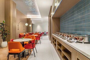 Un comedor moderno con mesas y sillas redondas, una barra de buffet y un elemento decorativo en el techo.