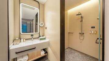 A hotel bathroom with a mirror, two sinks, a shower, and a towel rack.