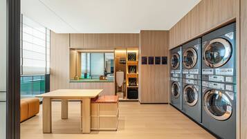 A modern laundry room with multiple washing machines, a wooden bench, and a table.