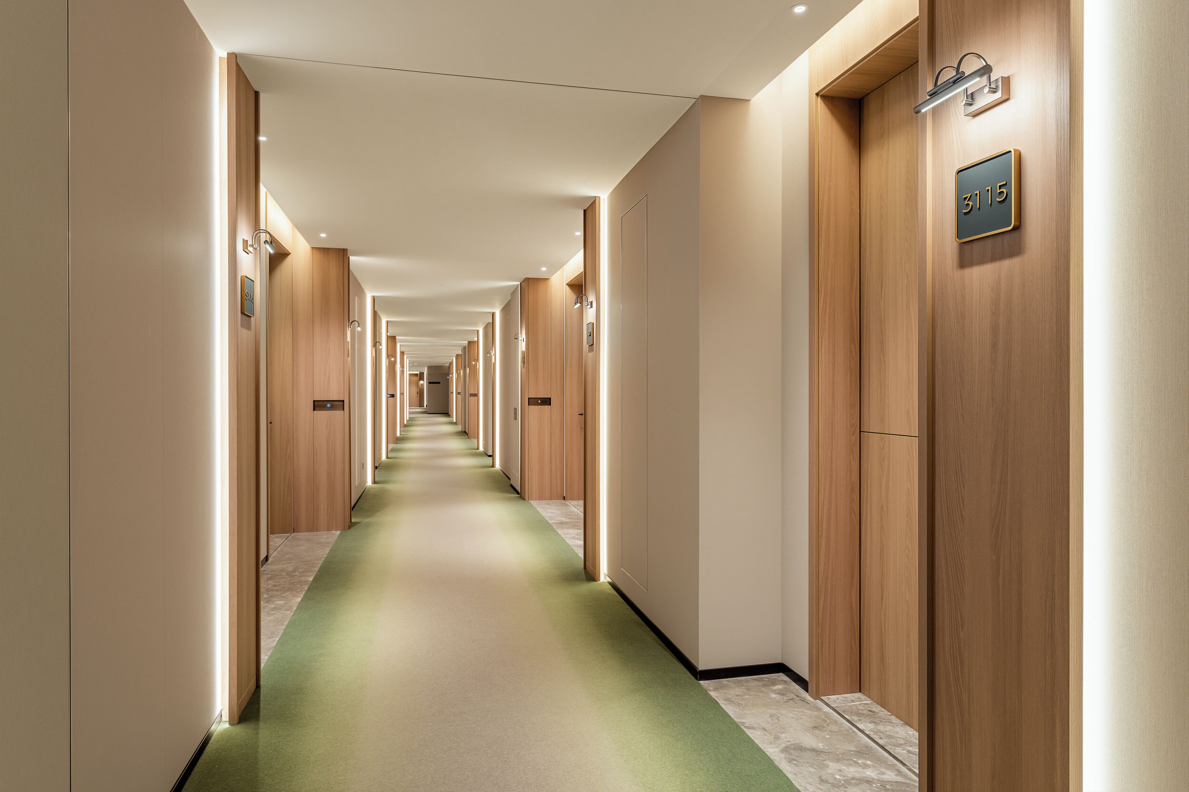 A hotel corridor with wooden doors, numbered room signs, and a green carpet.