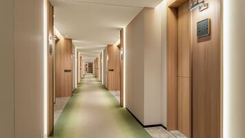 A hotel corridor with wooden doors, numbered room signs, and a green carpet.