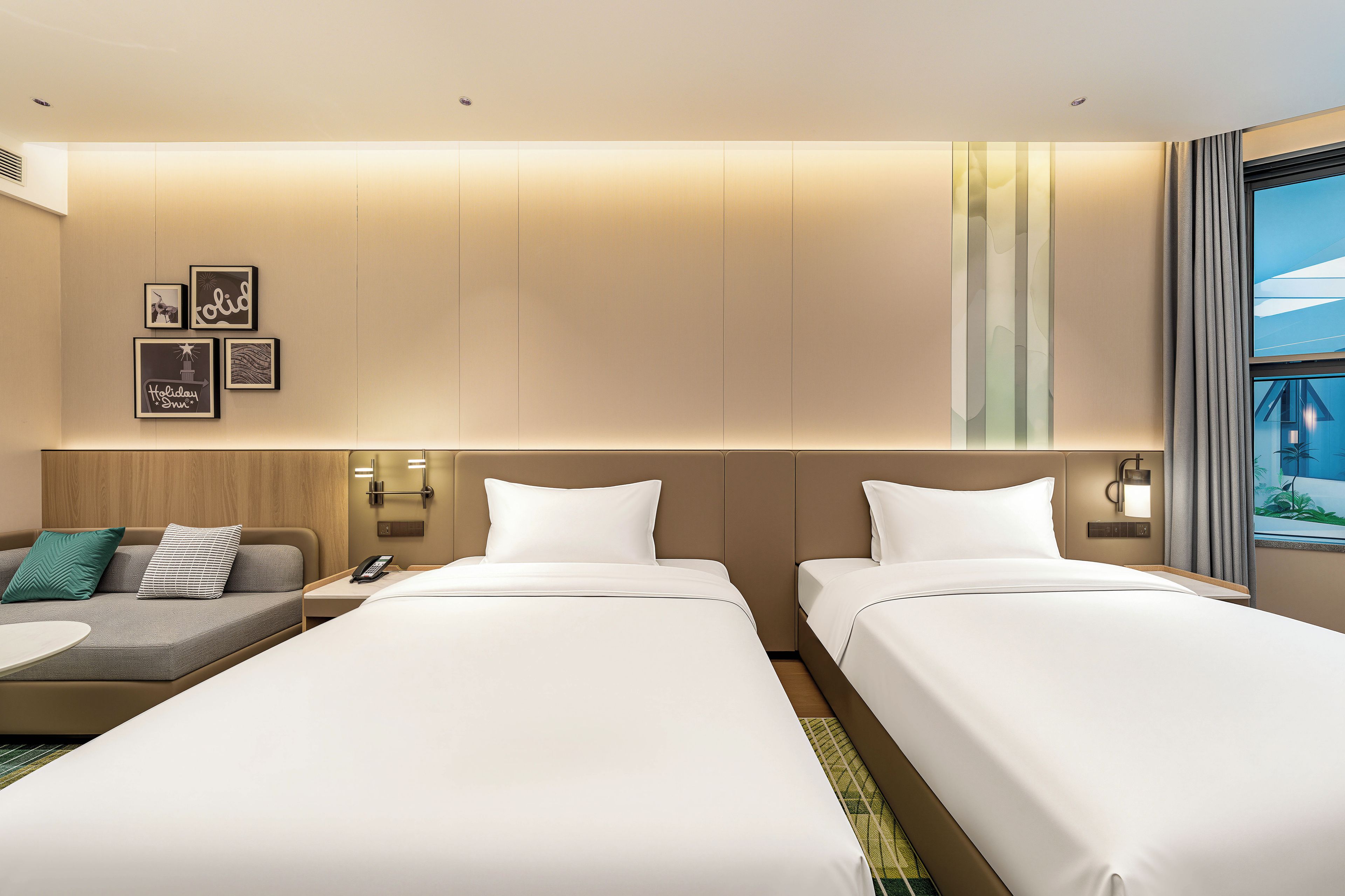A hotel room with two beds, a sofa, a small table, and a wall-mounted phone.