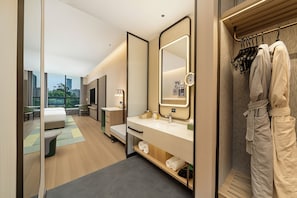 Une chambre d’hôtel moderne dotée d’un grand lit, d’un coin salon, d’une coiffeuse avec miroir et offrant une vue sur la ville.