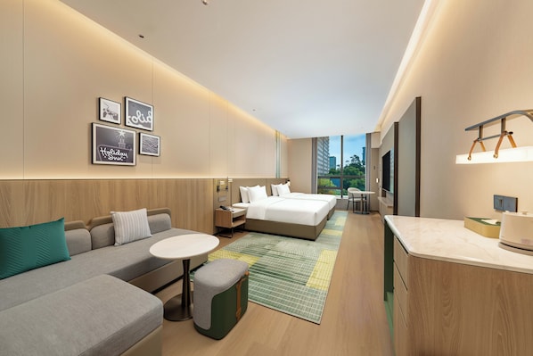 Una habitación de hotel moderna con sofá, cama, una mesita y un escritorio. Hay cuadros en la pared y una ventana con vistas a edificios.