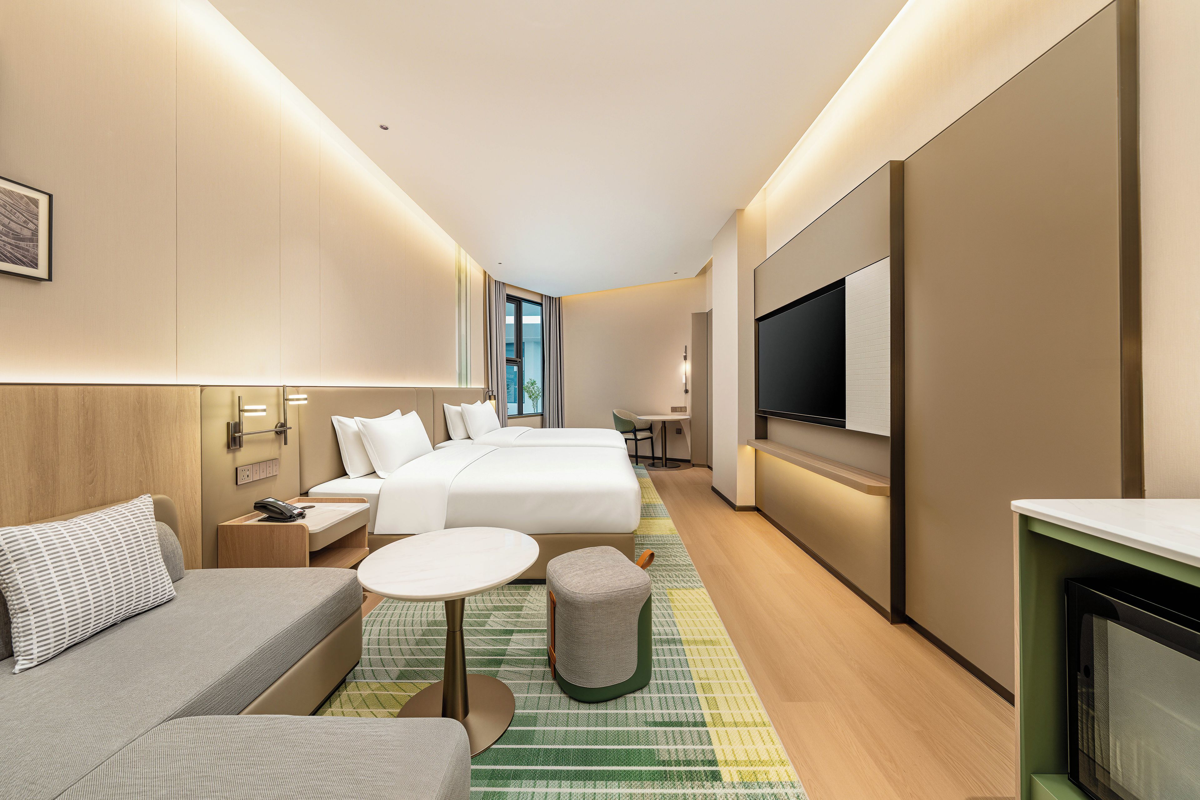 A hotel room with a bed, a sofa, a small table, a TV, and a view of the outdoors.