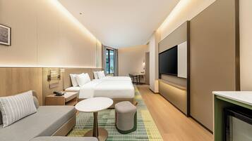 A hotel room with a bed, a sofa, a small table, a TV, and a view of the outdoors.