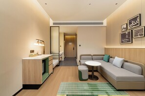 Habitación de hotel moderna con kitchenette, un sofá, una pequeña mesa y una alfombra verde a rayas.