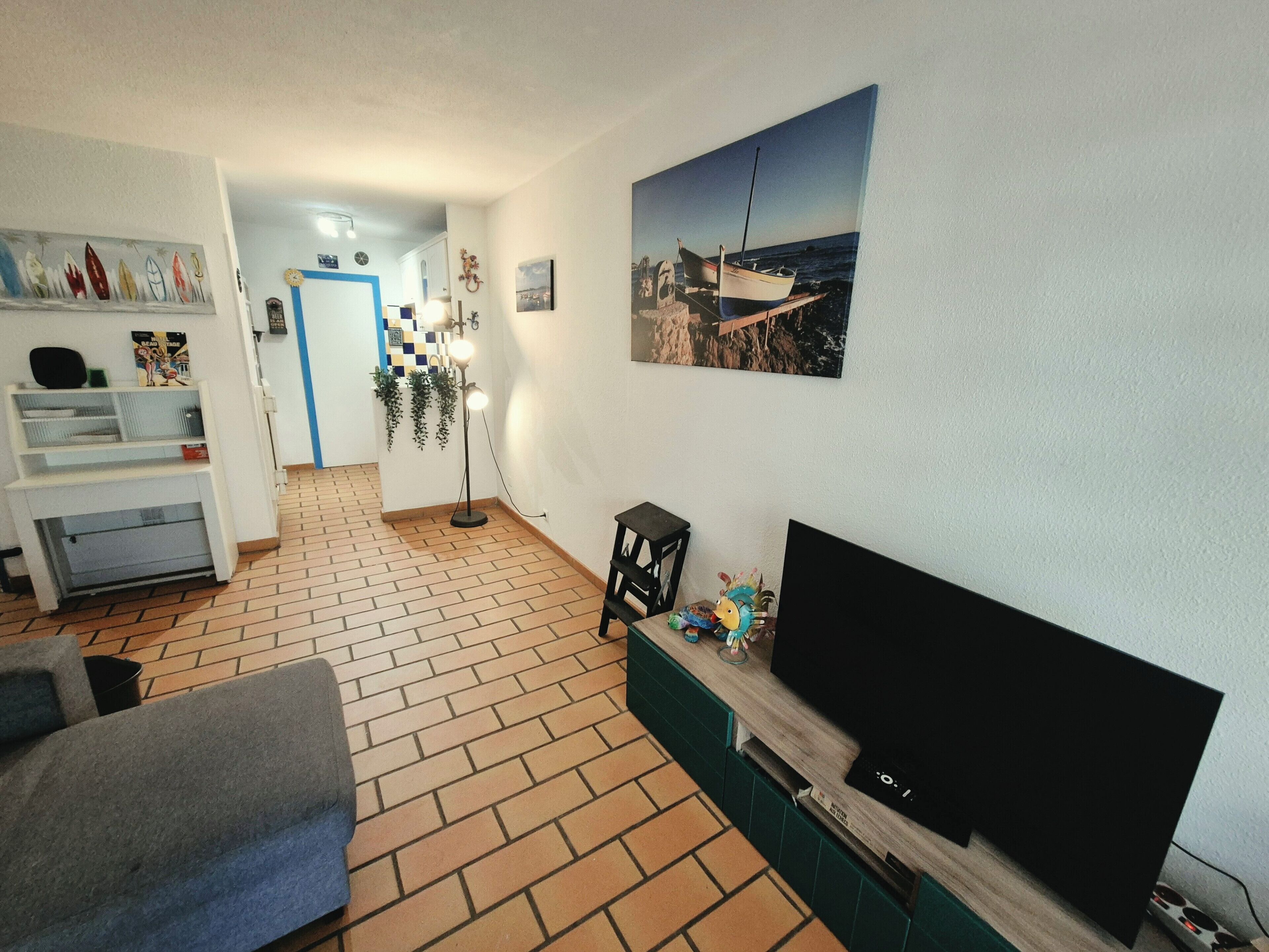 A living room with a flat-screen TV, a sofa, a coffee table, and a brick-patterned floor.