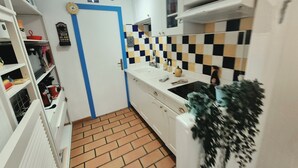 A compact kitchen with white cabinets, a checkered backsplash, and a tiled floor.