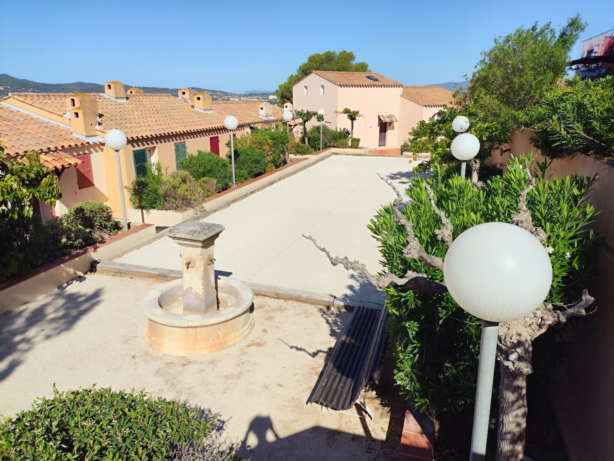 A rooftop terrace with a water fountain, potted plants, and a view of the surrounding buildings.
