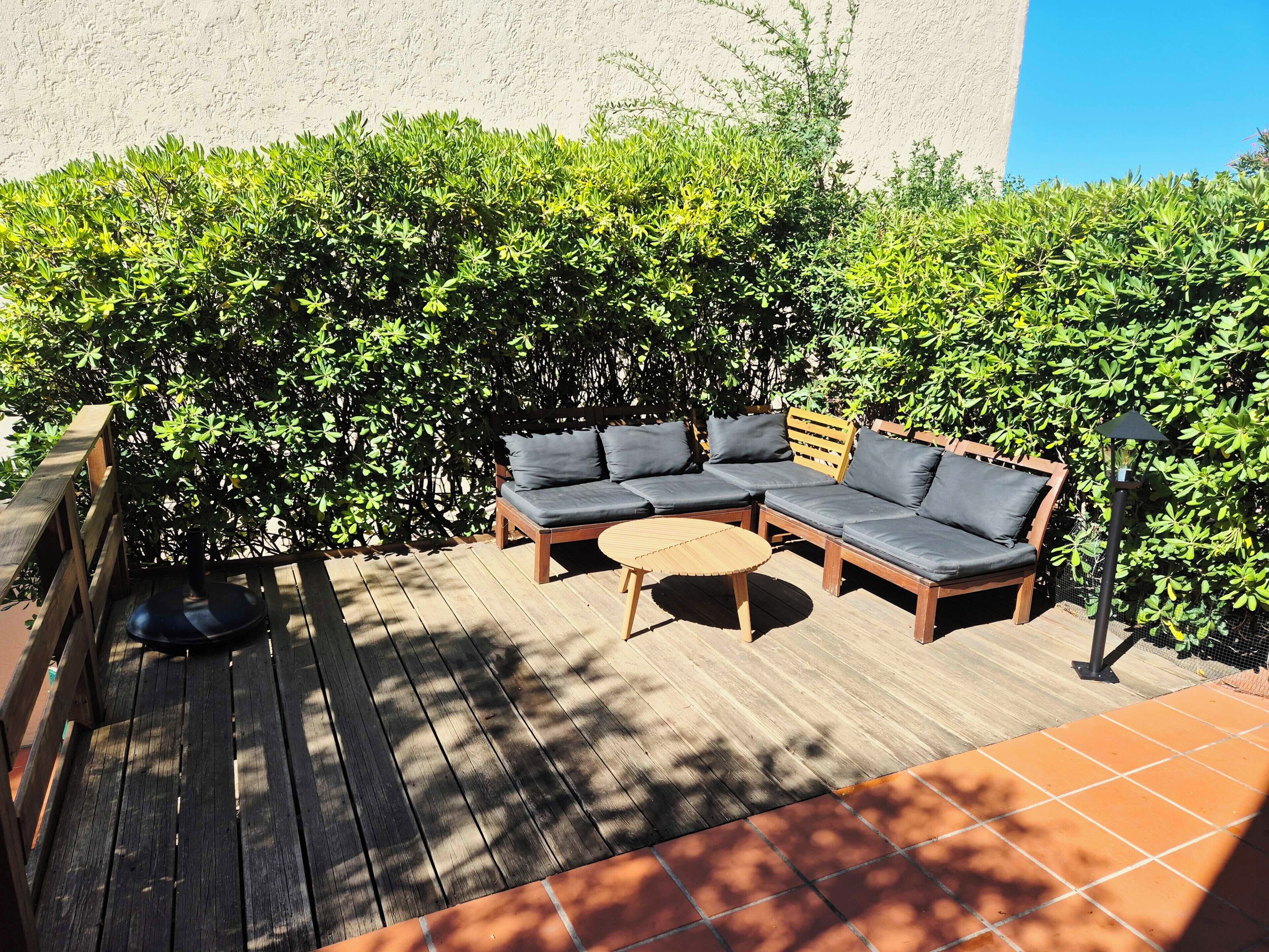 Une terrasse en bois avec un canapé et une petite table, entourée d’un feuillage verdoyant et luxuriant.