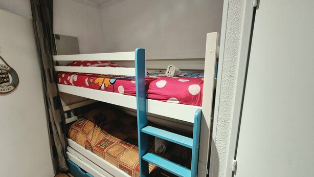 A bunk bed with a blue ladder, a red bedspread with white polka dots, and a patterned blanket.