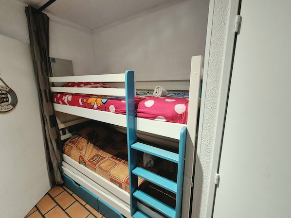 A bunk bed with a blue ladder, a red bedspread with white polka dots, and a patterned blanket.