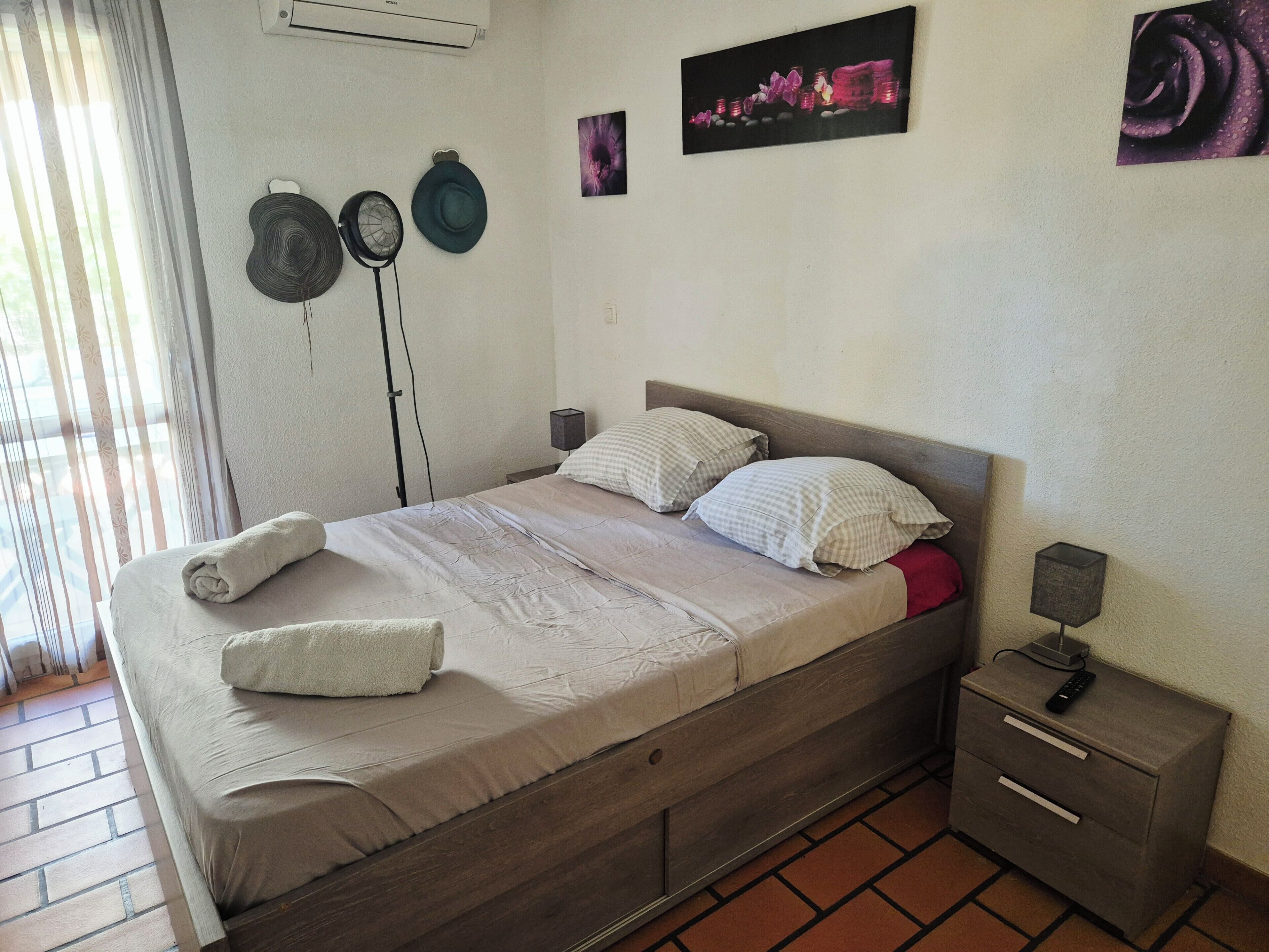 Ein ordentlich bezogenes Bett mit Kissen, ein Nachttisch mit Lampe und eine Wand-Klimaanlage.