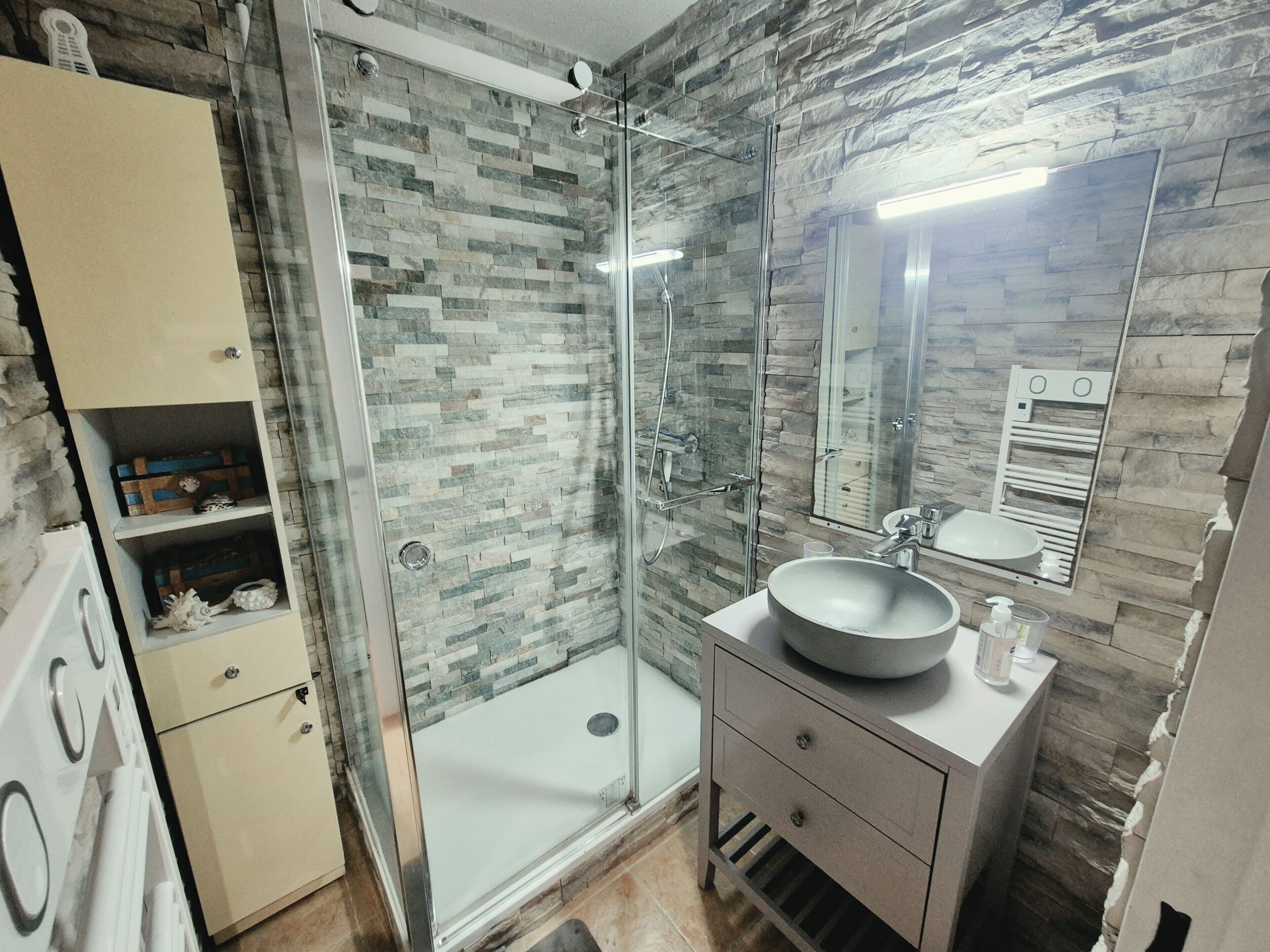 Une salle de bain avec une douche à parois de verre, un lavabo à cuve ronde et un miroir au-dessus du lavabo.