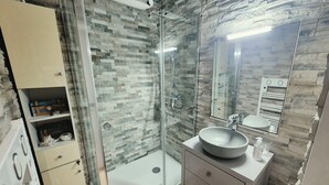 Een badkamer met een douche met glazen wanden, een wastafel met een rond bassin en een spiegel boven de wastafel.