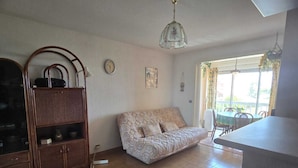 Un salon avec un canapé, un meuble en bois, une horloge et une fenêtre avec des rideaux.