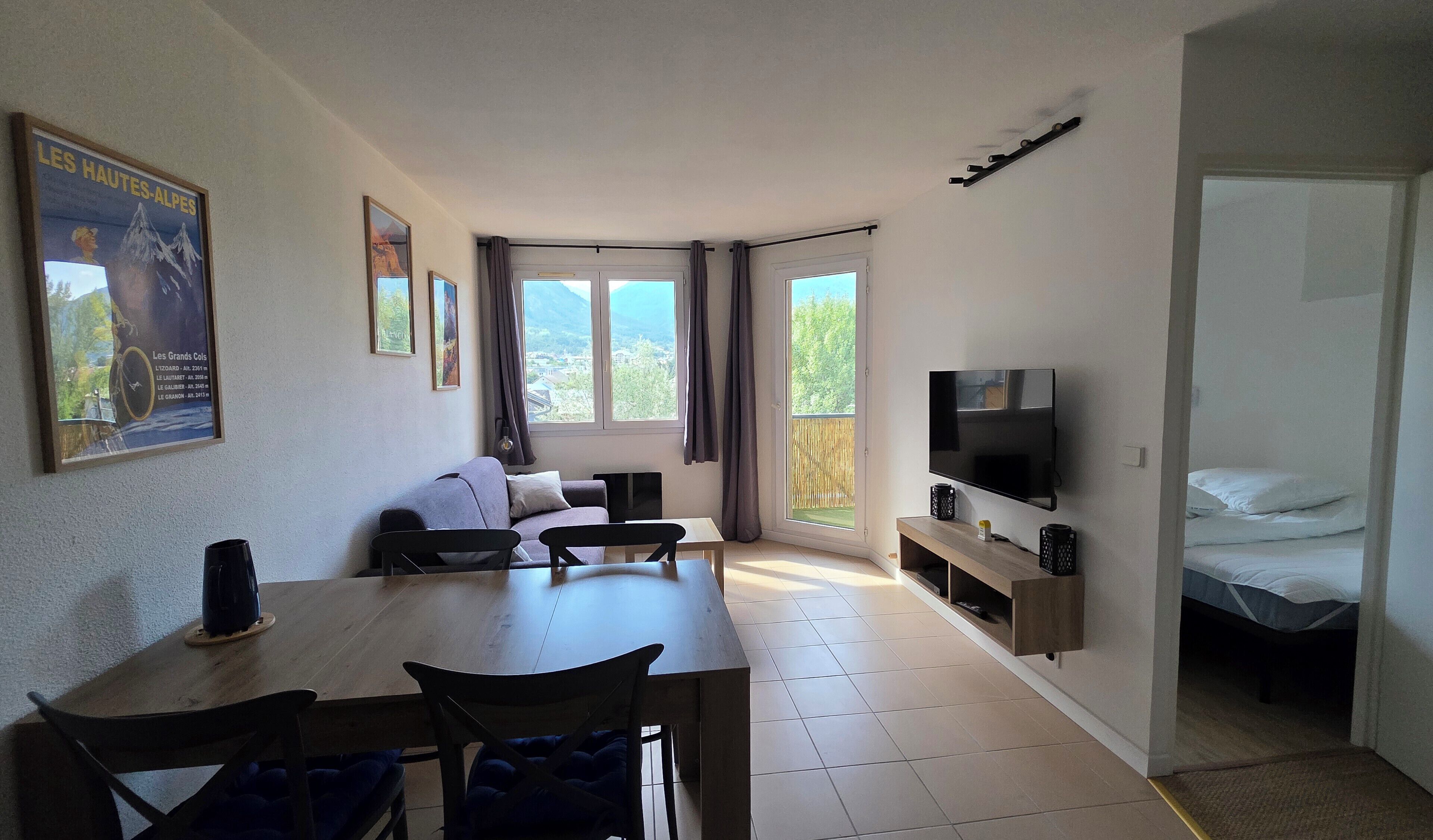 A room with a dining table, chairs, a sofa, a TV, and a bed.