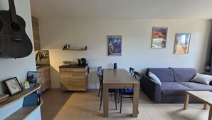 Ett vardagsrum med ett matbord, en soffa och en köksdel med en gitarr.