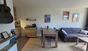 A living room with a dining table, a sofa, and a kitchen area with a guitar. - Apartment "Le Col de Mélodies" with balcony (Briançon)